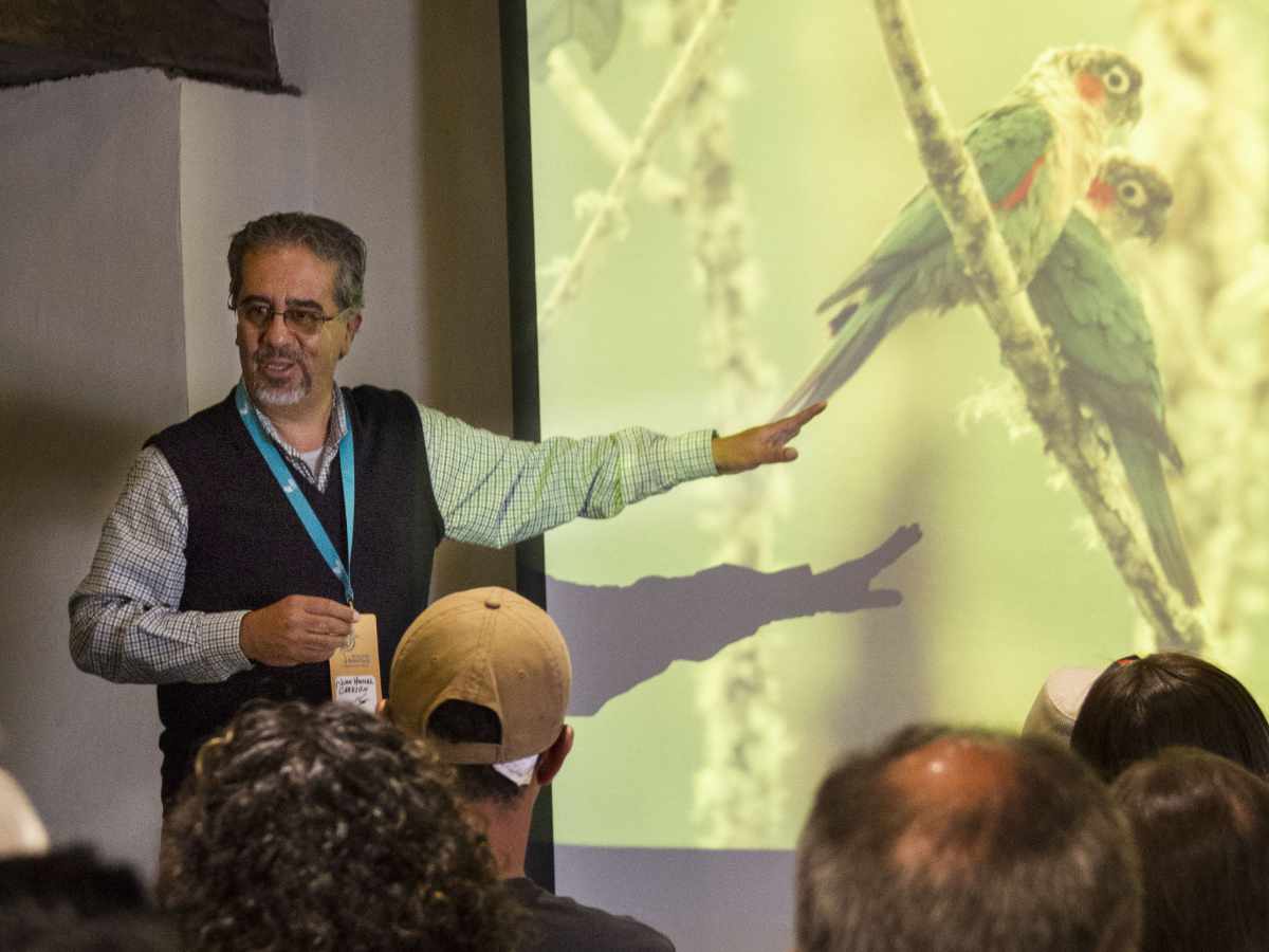 A man gives a keynote talk, featuring two parrots in a presentation, at the Ecuador Bird Fair in Cuenca in 2018